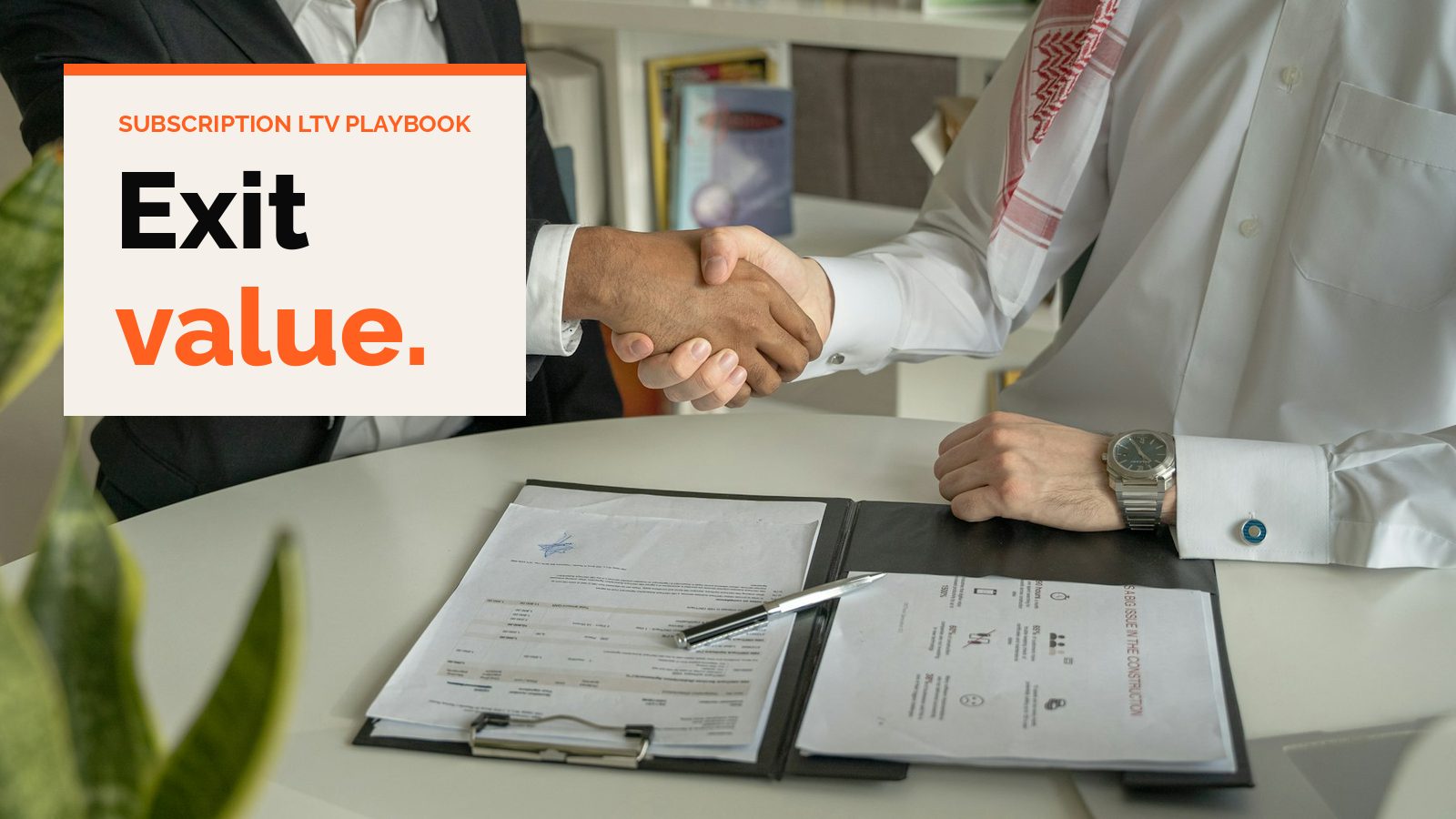 Two people shake hands over signed papers on a desk